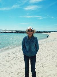 Portrait of smiling young woman standing at beach against sky