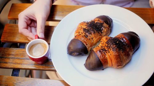 Close-up of croissants 2 pieces in dish and hand hold coffee cup on table