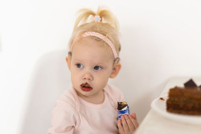 Portrait of cute girl eating food against white background