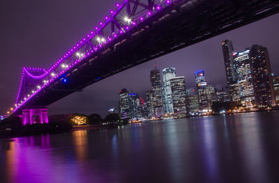 Low angle view of illuminated bridge over river in city at night