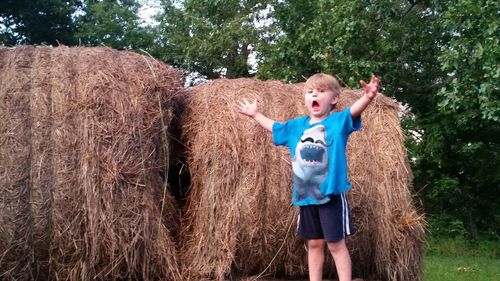 Portrait of boy standing by hay bale on field