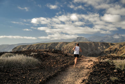 Rear view of man running on mountain against sky