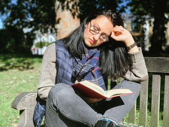 Young woman reads red book in park candid millennial girl in casual autumnal clothes siting on bench 