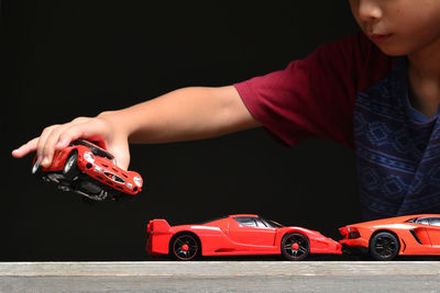 Midsection of boy playing with toy cars against black background