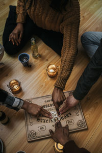 High angle view of multiracial friends using ouija board sitting on hardwood floor