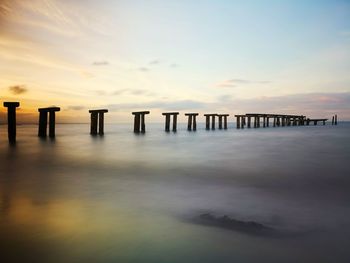 Wooden posts in sea against sky during sunset