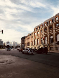 Cars on road by buildings against sky in city