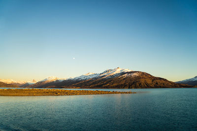 Scenic view of lake and mountains against clear blue sky