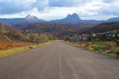 Empty road leading towards mountains against sky