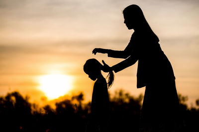 Silhouette of mother and daughter on field at sunset