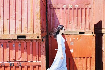 Side view of young woman walking by cargo containers