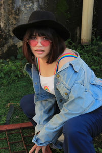 Portrait of young woman wearing sunglasses and hat crouching outdoors