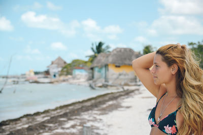 Young woman in bikini looking away at beach against sky