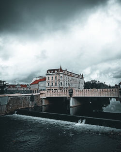 View of building by river against cloudy sky