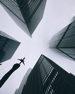 Cropped hand holding toy airplane amidst skyscrapers against sky