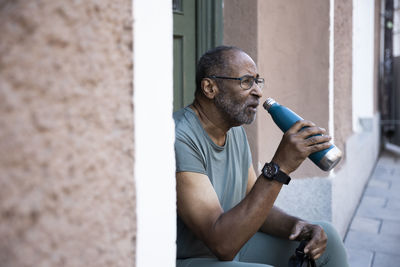 Senior man drinking water from bottle outside house