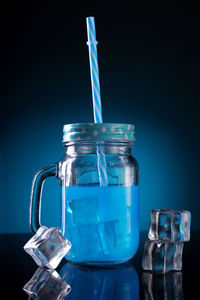 Blue colored cocktail in a mason jar with straw and ice cubes