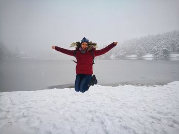 Full length of smiling young woman jumping over snow against sky