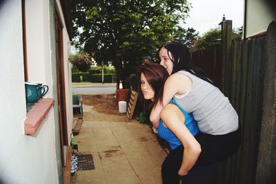 Portrait of young woman piggybacking sibling while standing outdoors