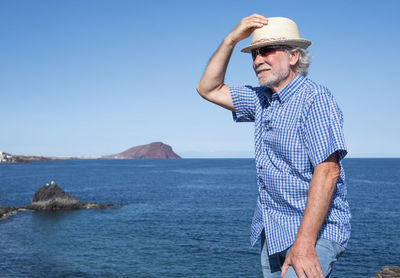 Man wearing hat standing by sea against sky