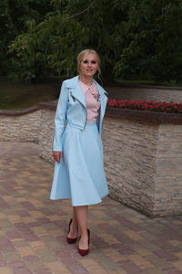 Portrait of young woman in dress standing against trees at park