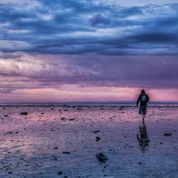Silhouette person walking on beach against sky during sunset