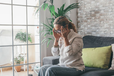 Side view of woman using mobile phone while sitting on sofa at home