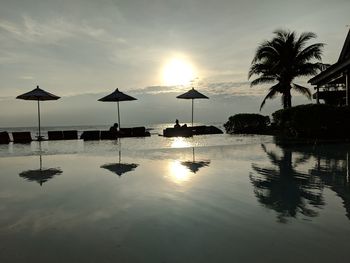 Silhouette swimming pool by sea against sky during sunset
