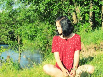 Young woman sitting on grass against trees