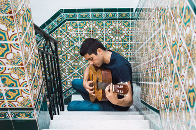 Young man playing guitar against wall