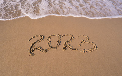 Hand-drawn numbers 2023 of new year on wet yellow sand on beach, copy space