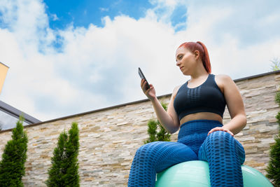 Low angle view of young man sitting against sky