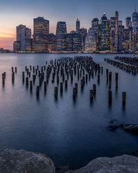 Wooden posts in sea against sky at sunset