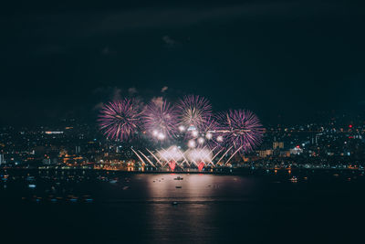 Firework display over illuminated city against sky at night