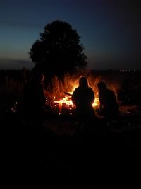 Silhouette people sitting by bonfire against sky at night