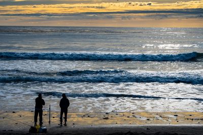 Silhouette people standing on beach against sky during sunset