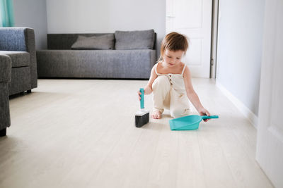 Cute european child with blue scoop for garbage and brush for sweeping floor 