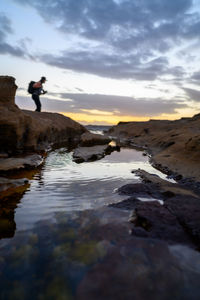 Man standing on rock against sky during sunset