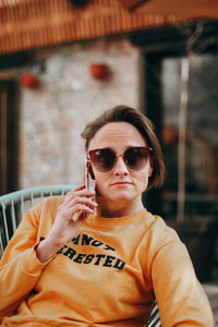 Beautiful young woman with short blond hair in casual clothing sitting and holding mobile phone.