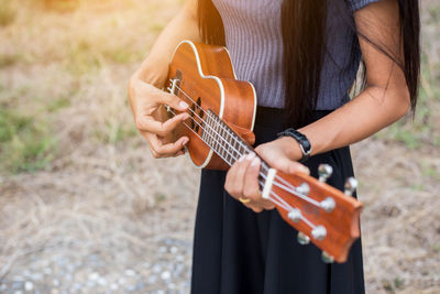 Midsection of woman playing guitar on field