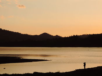 Scenic view of silhouette mountains by lake during sunset