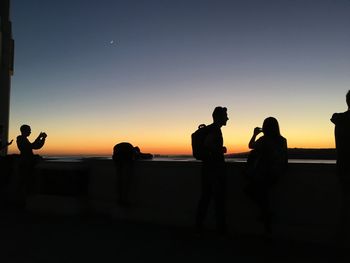 Silhouette people photographing on beach against clear sky during sunset