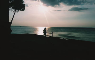 Silhouette man standing on beach against sky during sunset