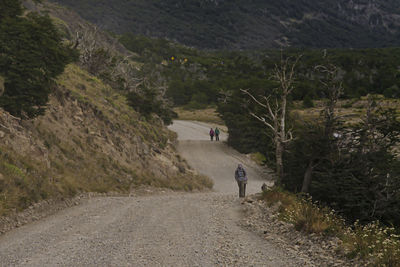 Rear view of people walking on road by mountain