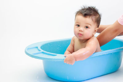 Cropped hands touching cute baby boy in bathtub against white background