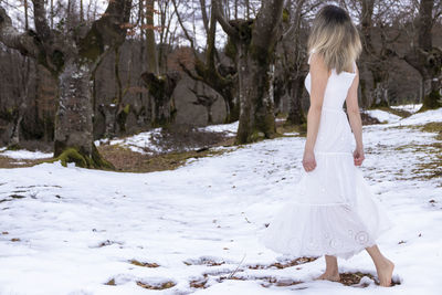 Woman in a white dress walking through a snowy forest, creating a dreamlike and surreal atmosphere