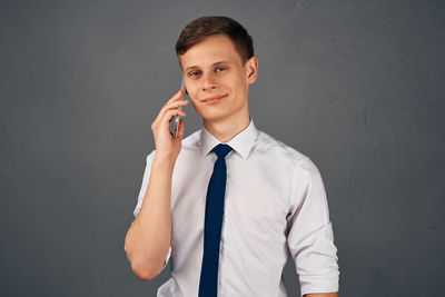 Portrait of young man holding camera while standing against gray background