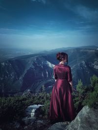 Rear view of woman standing on cliff against sky