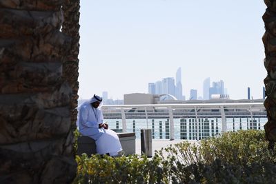 Man wearing dish dash sitting by river in city