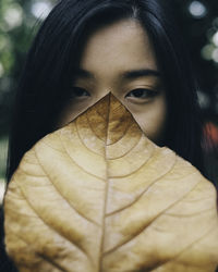 Portrait of young woman hiding face with autumn leaf
